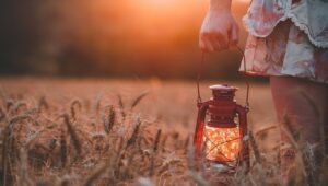 Vrouw met lantaarn in weiland bij zonsondergang