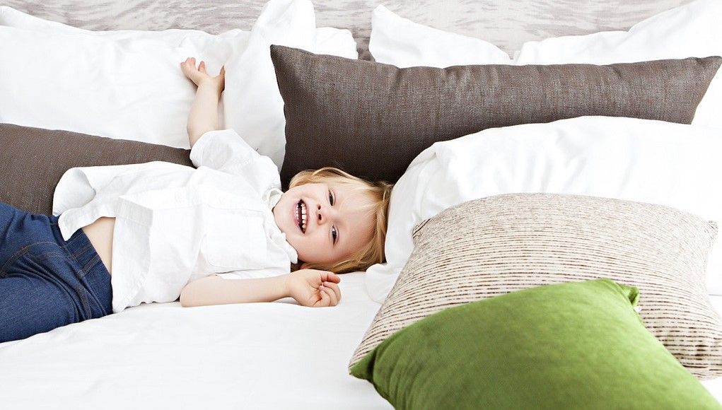 Klein jongetje speelt in het bed van zijn ouders omringd door sierkussens