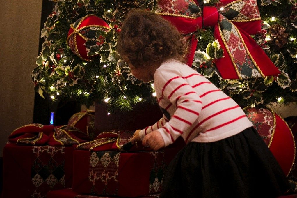 Klein meisje bekijkt de cadeautjes onder de kerstboom tijdens het kerstdiner