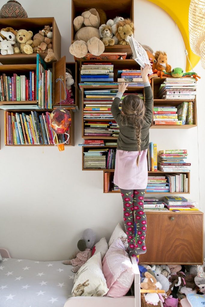 Klein meisje staat op haar tenen om een boek uit de kast te kunnen pakken